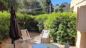 A patio with a round table and four chairs, surrounded by stone tiles and greenery. - 2 People | Near town center and beaches | Air-conditioned | Garden (Cavalaire sur Mer)
