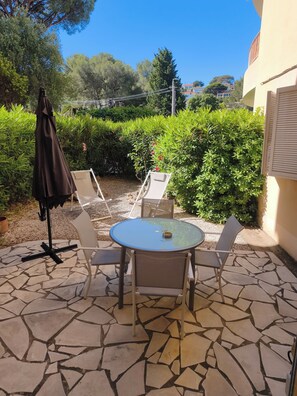 A patio with a round table and four chairs, surrounded by stone tiles and greenery. - 2 People | Near town center and beaches | Air-conditioned | Garden (Cavalaire sur Mer)