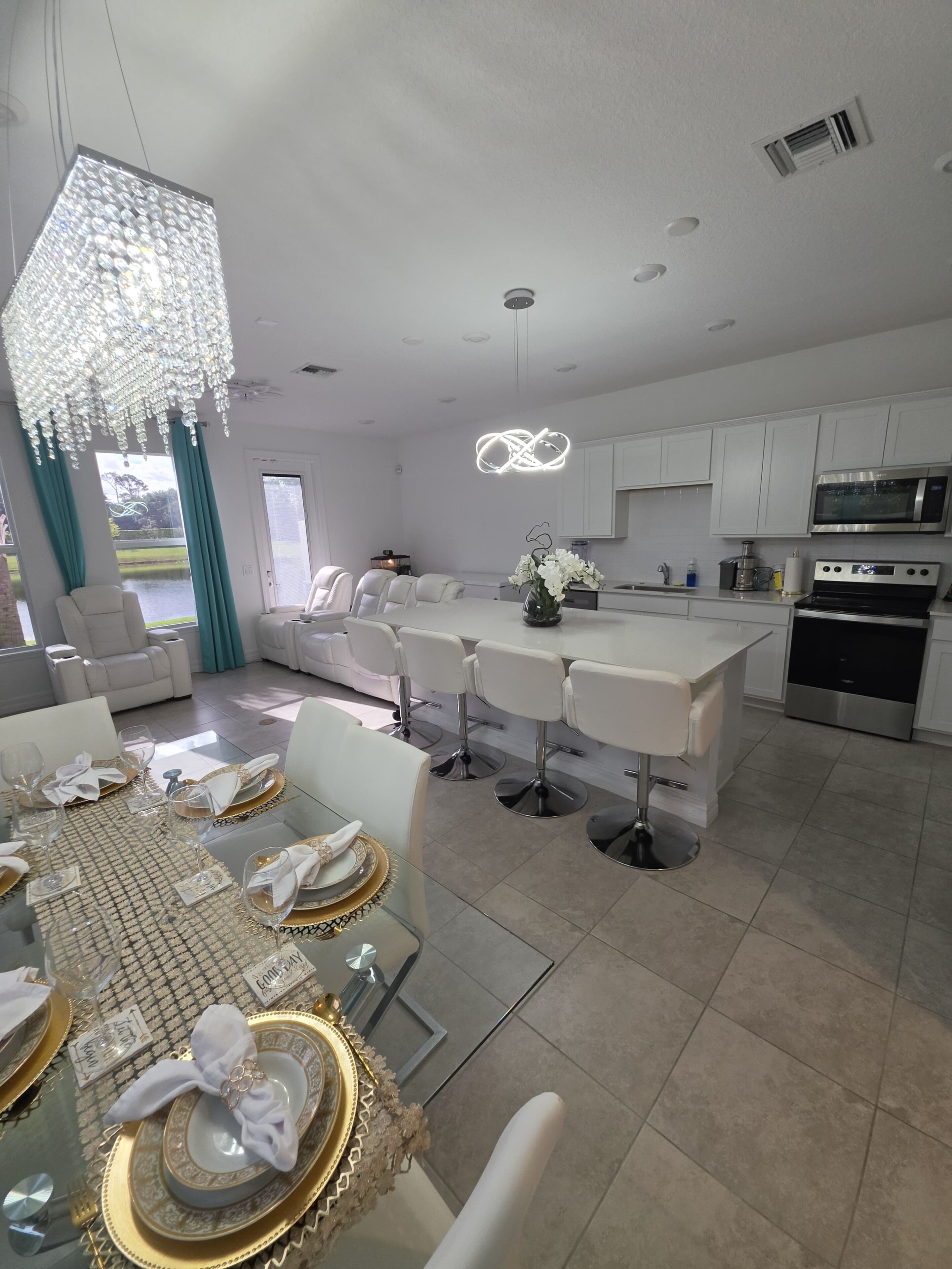 A modern kitchen with white cabinetry, a central island with bar stools, and a dining area with a glass table set for six.