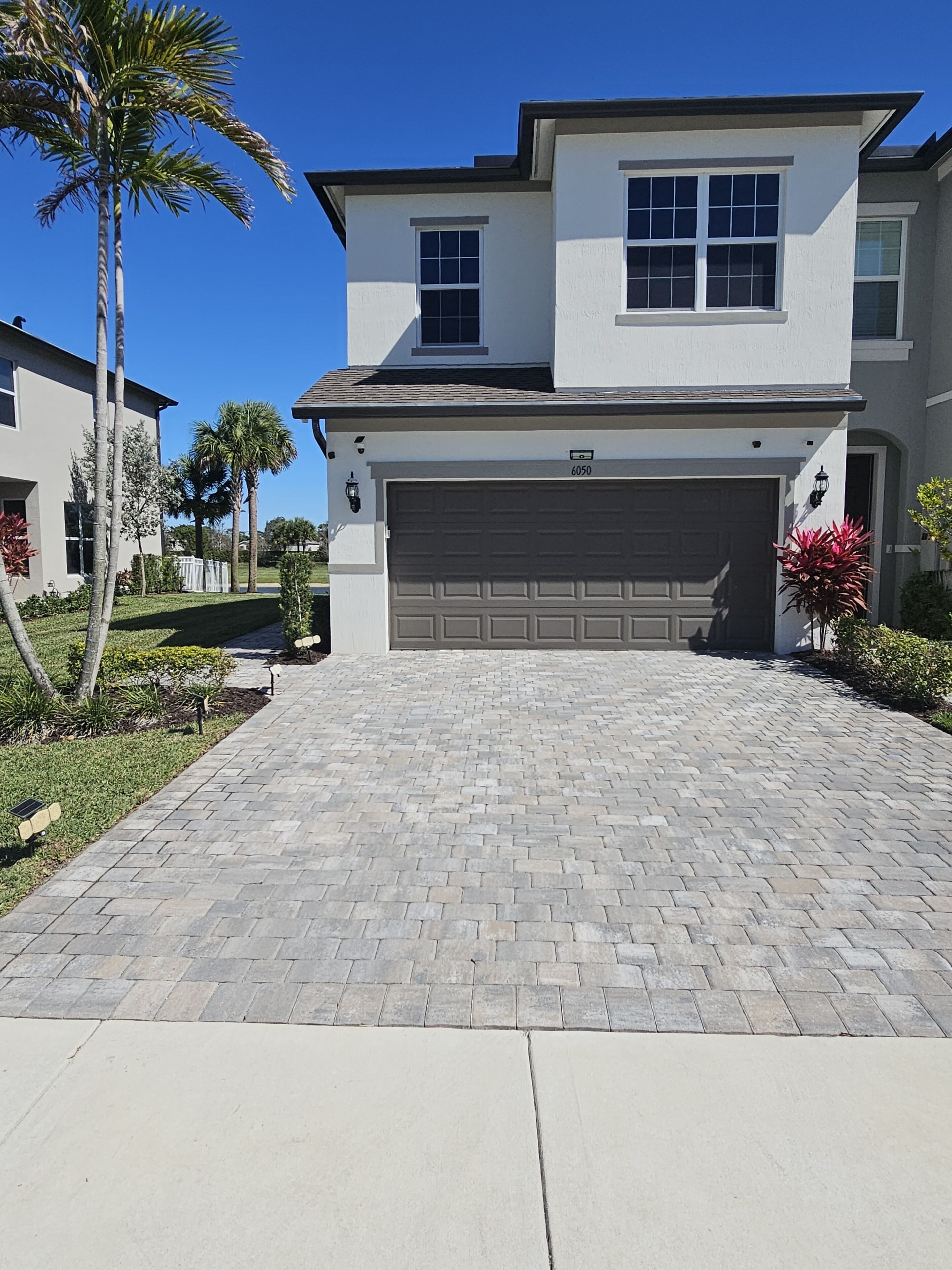 Ein zweistöckiges Haus mit Garage, befestigter Auffahrt und einem gepflegten Rasen mit Palmen.