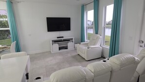 Ein modernes Wohnzimmer mit einem Flachbildfernseher, einem weißen Sofa, einem weißen Couchtisch und Blick auf ein Gewässer durch große Fenster.