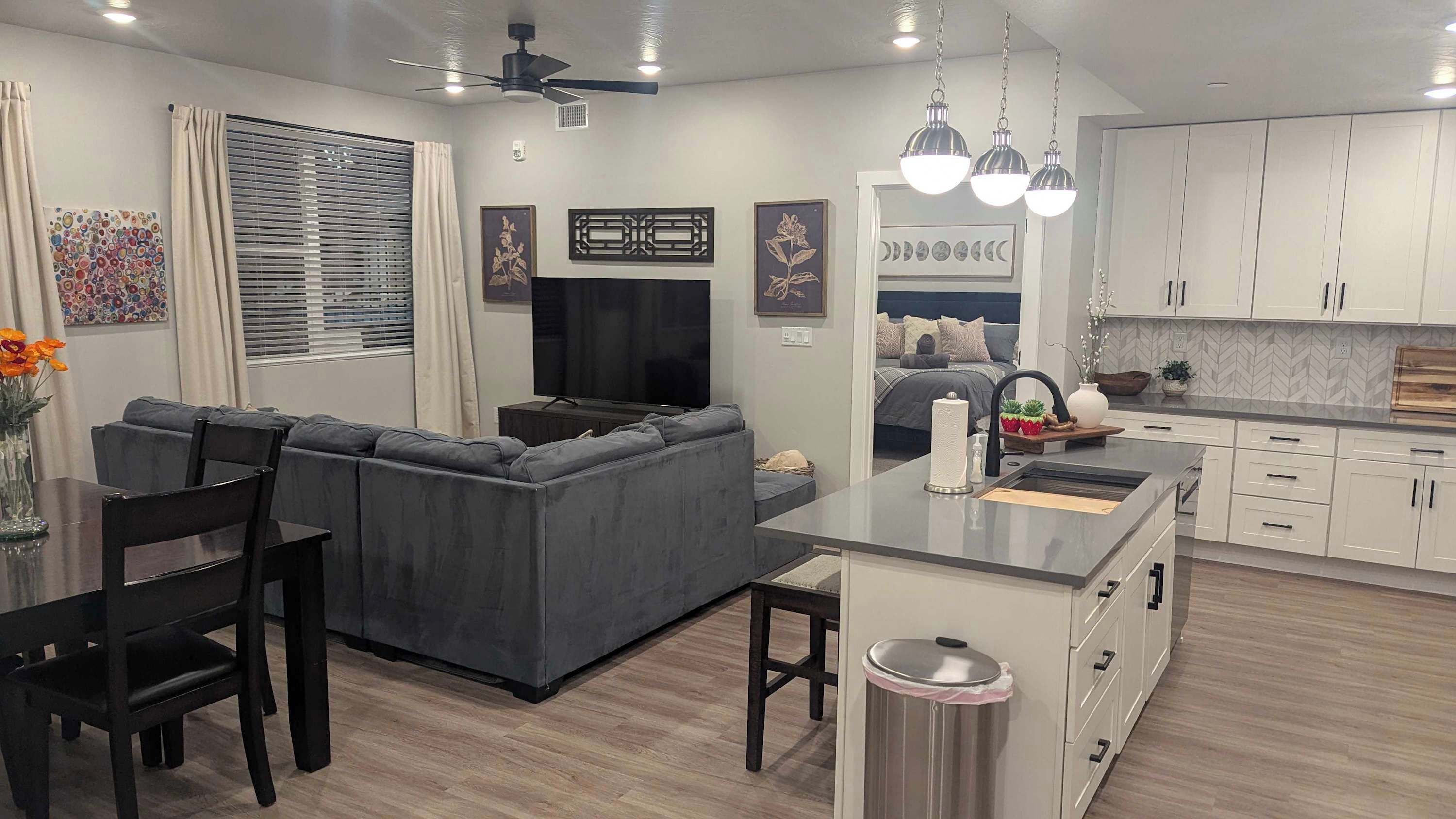 A modern kitchen with white cabinets, a central island, and a dining area with a gray sofa and black chairs.