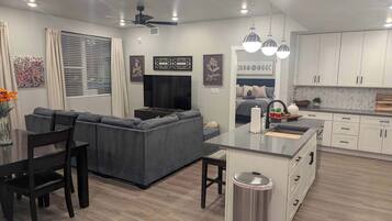 A modern kitchen with white cabinets, a central island, and a dining area with a gray sofa and black chairs.