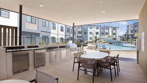 Une terrasse extérieure avec un barbecue, des sièges et une vue sur la piscine.