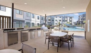 Een terras buiten met een barbecue, zitplaatsen en uitzicht op een zwembad.