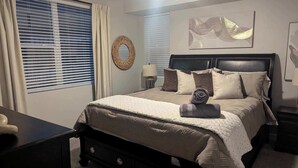 Une chambre à coucher bien rangée, avec un lit, des tables de chevet, une lampe et une œuvre d’art accrochée au mur.
