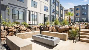 A modern outdoor seating area with a fire feature, stone walls, and a staircase leading to a building with multiple windows.