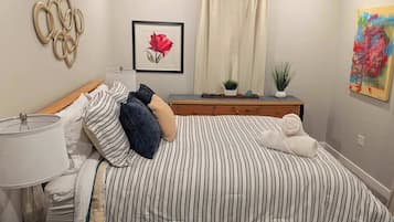 A neatly arranged bedroom with a striped bed, bedside table, lamp, and a framed picture of a rose.