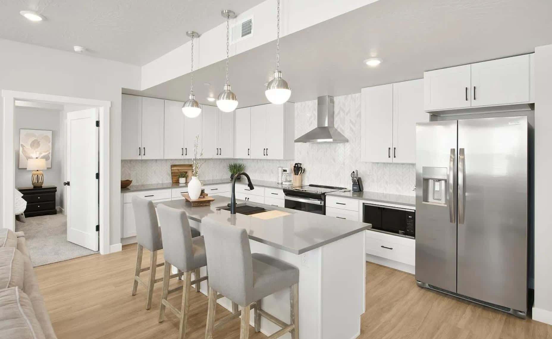 A modern kitchen with white cabinets, a stainless steel refrigerator, and a central island with bar stools.