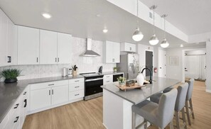 Cozinha moderna com armários brancos, uma ilha central e iluminação pendente.