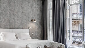 Ein Schlafzimmer mit einem großen Bett, einem Sofa, einem Fenster mit Vorhängen und einer Wandleuchte.