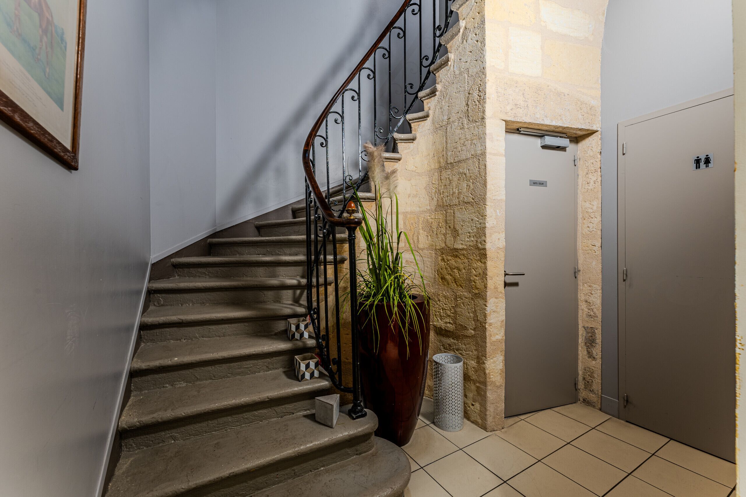 Un escalier avec une rampe en métal, un pot de fleurs, une poubelle et une porte avec une pancarte.