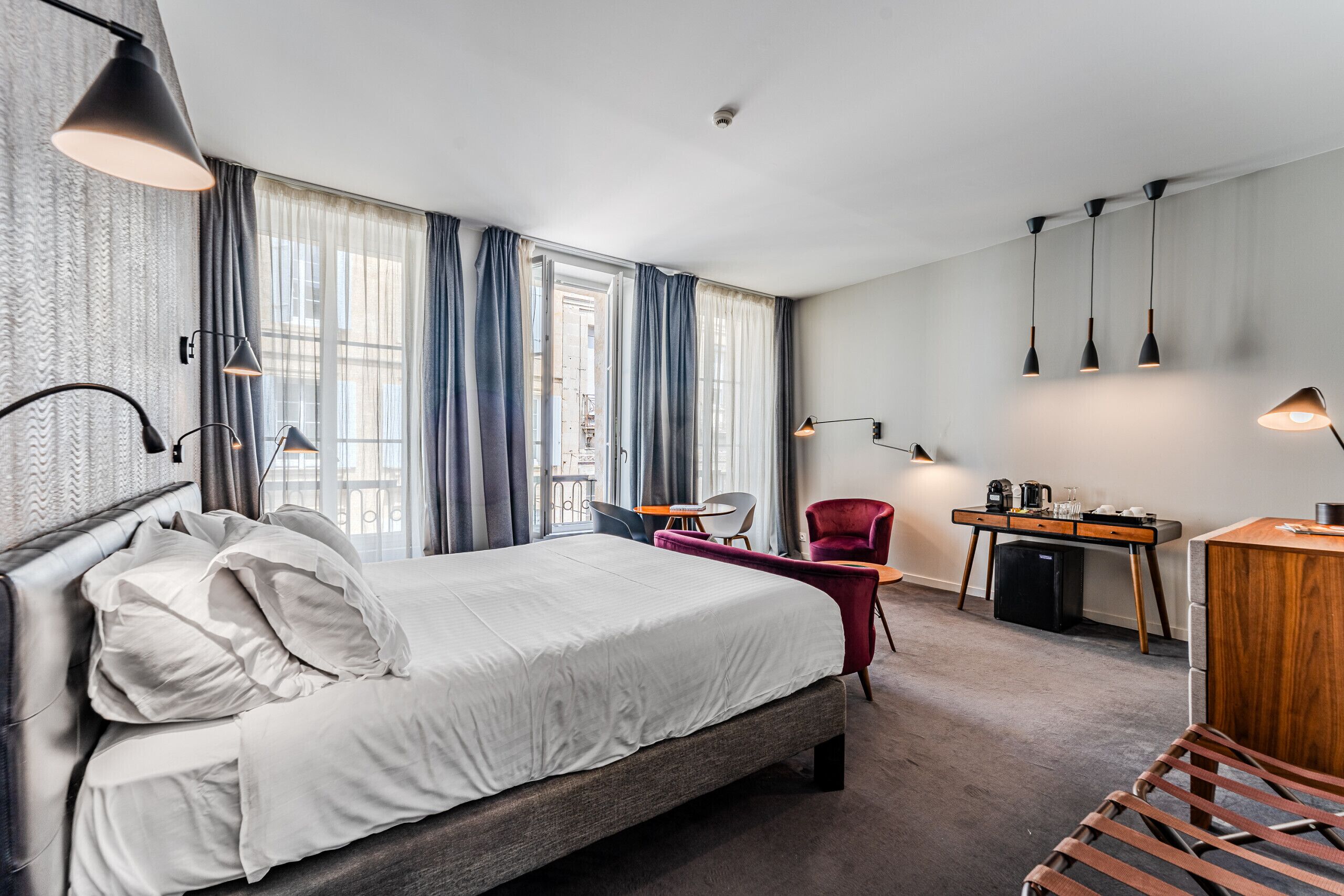 A modern hotel room with a large bed, a desk, a chair, and a small table.