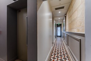 Een gang met een zwart-wit geruite vloer, een deur aan de linkerkant en een muur met een reliëf aan de rechterkant.