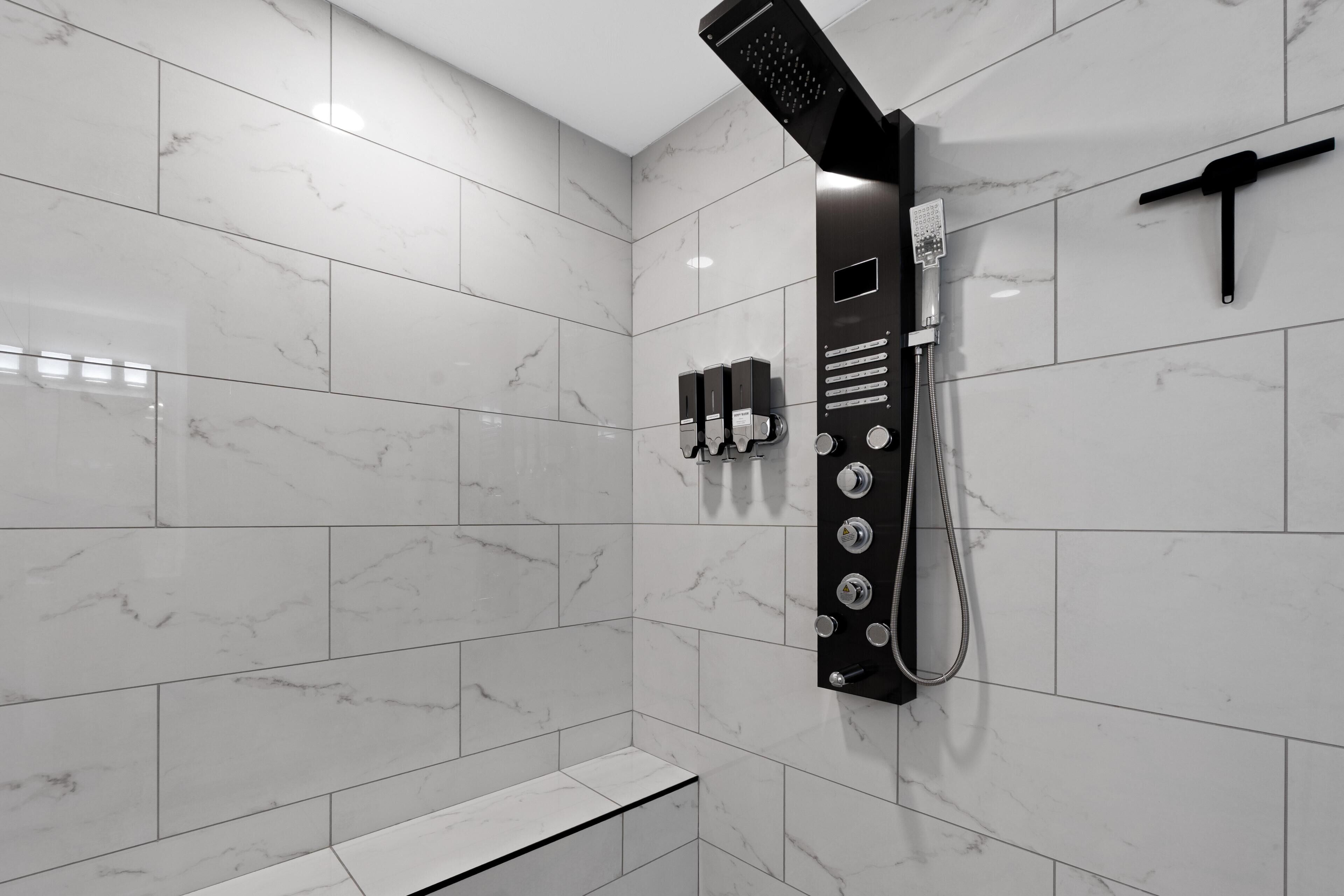 A modern bathroom with white marble tiles, a wall-mounted shower, and a bench.