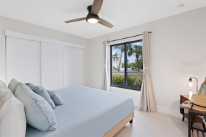 Ein Schlafzimmer mit Bett, Deckenventilator, Fenster mit Vorhängen und Nachttisch mit Lampe.