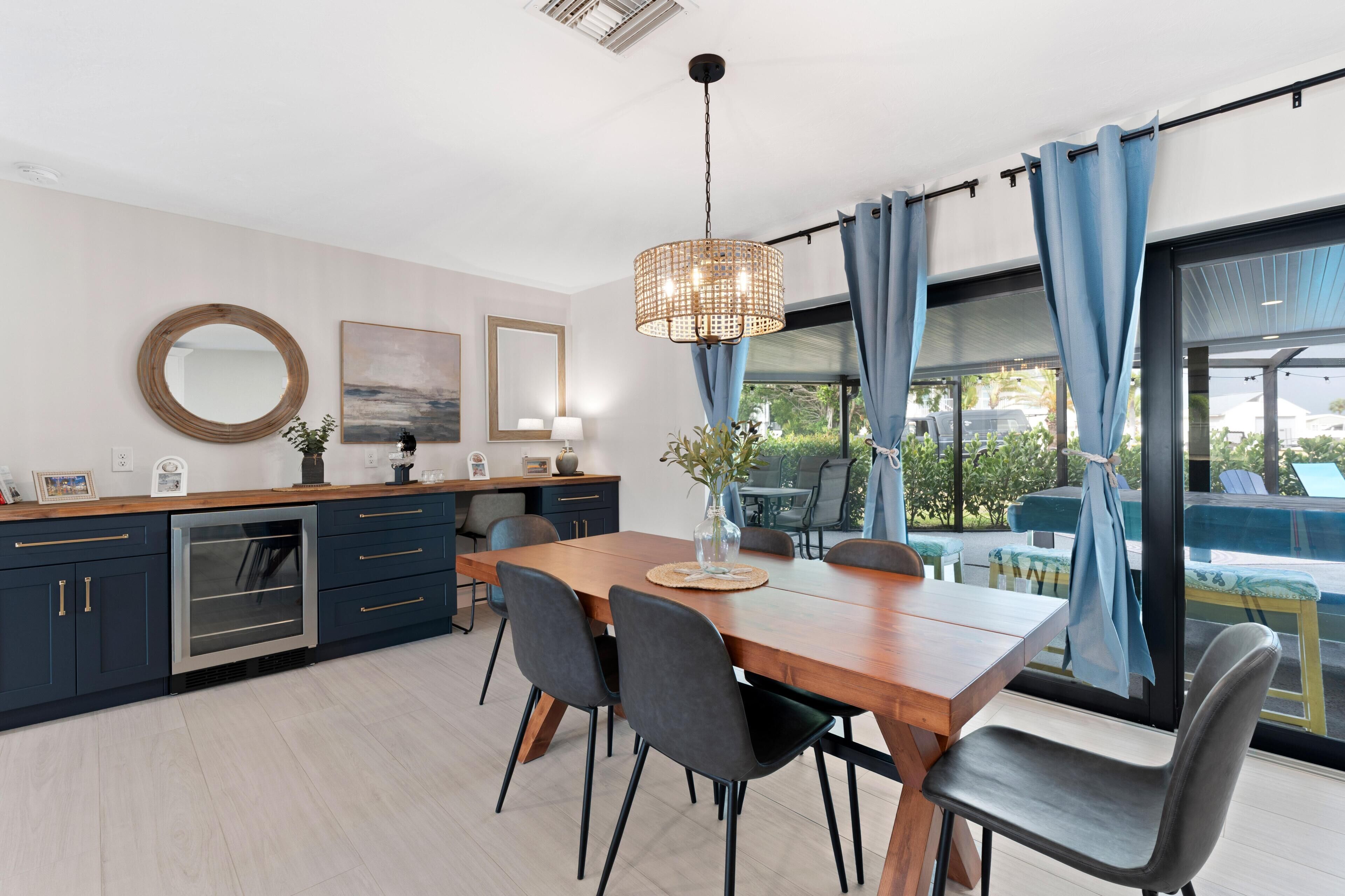 A modern kitchen with dark cabinetry, a wooden dining table, and a large window with blue curtains.