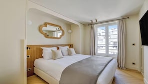 Un dormitorio con cama, espejo, ventana con cortinas y vista a edificios.