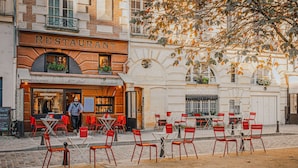 Un restaurant avec une terrasse, un homme qui passe, et une rue pavée.