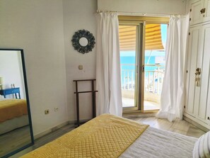 A bedroom with a bed, a mirror, a wardrobe, a small table, and a view of the sea through a balcony. - Apartment in front of the sea with beautiful views. The beach just below (Fuengirola)