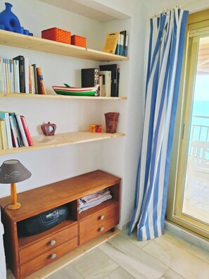 A room with a wooden bookshelf, a small table with a lamp, and a window with a striped curtain. - Apartment in front of the sea with beautiful views. The beach just below (Fuengirola)