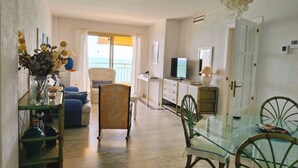 Un amplio salón con balcón, una mesa de comedor y un televisor.