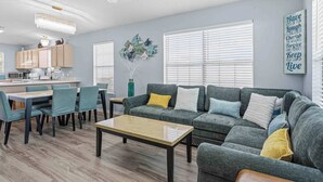 A modern living room with a sofa, chairs, a coffee table, and a kitchen in the background. - Relax on Navarre Beach, Play in Pensacola (Gulf Breeze)