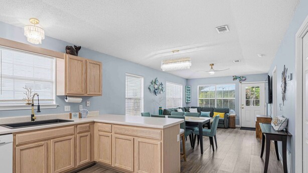 A modern kitchen with wooden cabinets, a central island, and a dining area with a table and chairs. - Relax on Navarre Beach, Play in Pensacola (Gulf Breeze)