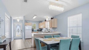 A modern kitchen with wooden cabinets, a dining area with teal chairs, and a chandelier. - Relax on Navarre Beach, Play in Pensacola (Gulf Breeze)