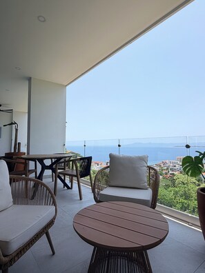 A balcony with wicker furniture, a round table, and a view of the sea and cityscape. - Tropical Luxury (Puerto Vallarta)