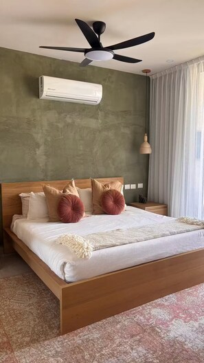 Ein Schlafzimmer mit Bett, Deckenventilator, Klimaanlage, Nachttischlampe und einem Fenster mit Vorhängen.