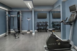 Uma academia com esteira, banco de musculação e pesos livres.