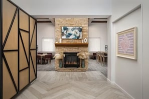 Quarto com lareira, piso de madeira em padrão herringbone, área de jantar e pintura abstrata emoldurada na parede.