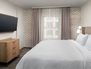 Une chambre d’hôtel avec un lit, une commode en bois, un téléviseur fixé au mur et un mur décoré d’un motif en briques.