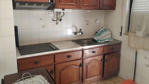 Cozinha com armários de madeira, pia, fogão e janela com persianas.