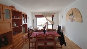Uma área de refeições com uma mesa e cadeiras de madeira, um armário com portas de vidro, uma televisão e um leque decorativo na parede.