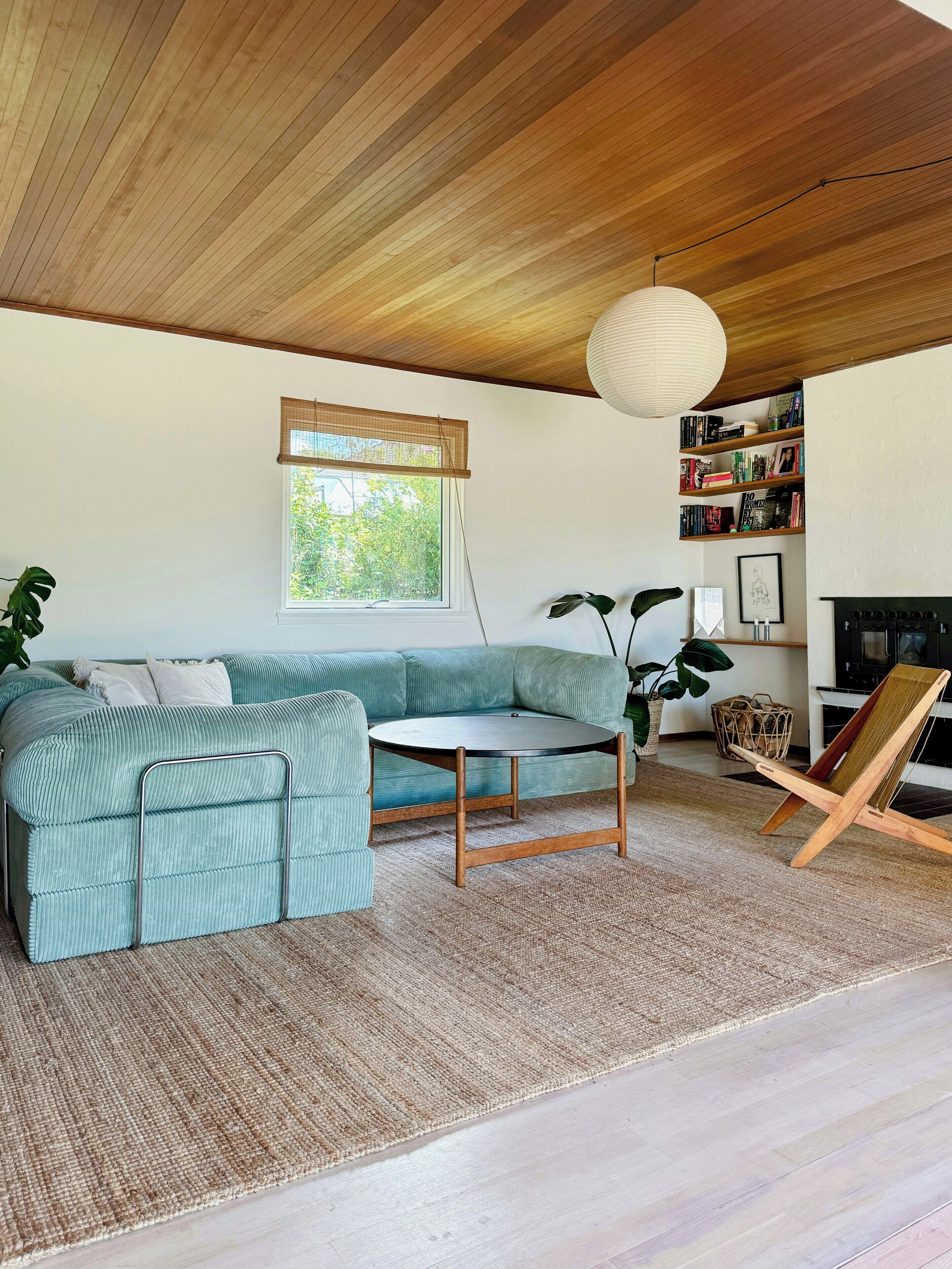 Ein Wohnzimmer mit Ecksofa, rundem Couchtisch, Holzboden, Bücherregal und Kamin.
