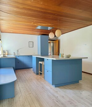Eine moderne Küche mit blauen Schränken, einer Holzbalkendecke und Pendelleuchten.