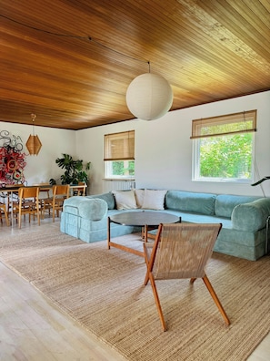 Ein modernes Wohnzimmer mit Holzboden, einem runden Tisch, einem blauen Sofa und einem Essbereich mit Holzstühlen.
