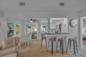 A modern kitchen with a central island, bar stools, and a dining area with a sofa and chairs. - 3BR Home, Indoor Pool, Hot Tub, Dog Friendly (Gulf Breeze)