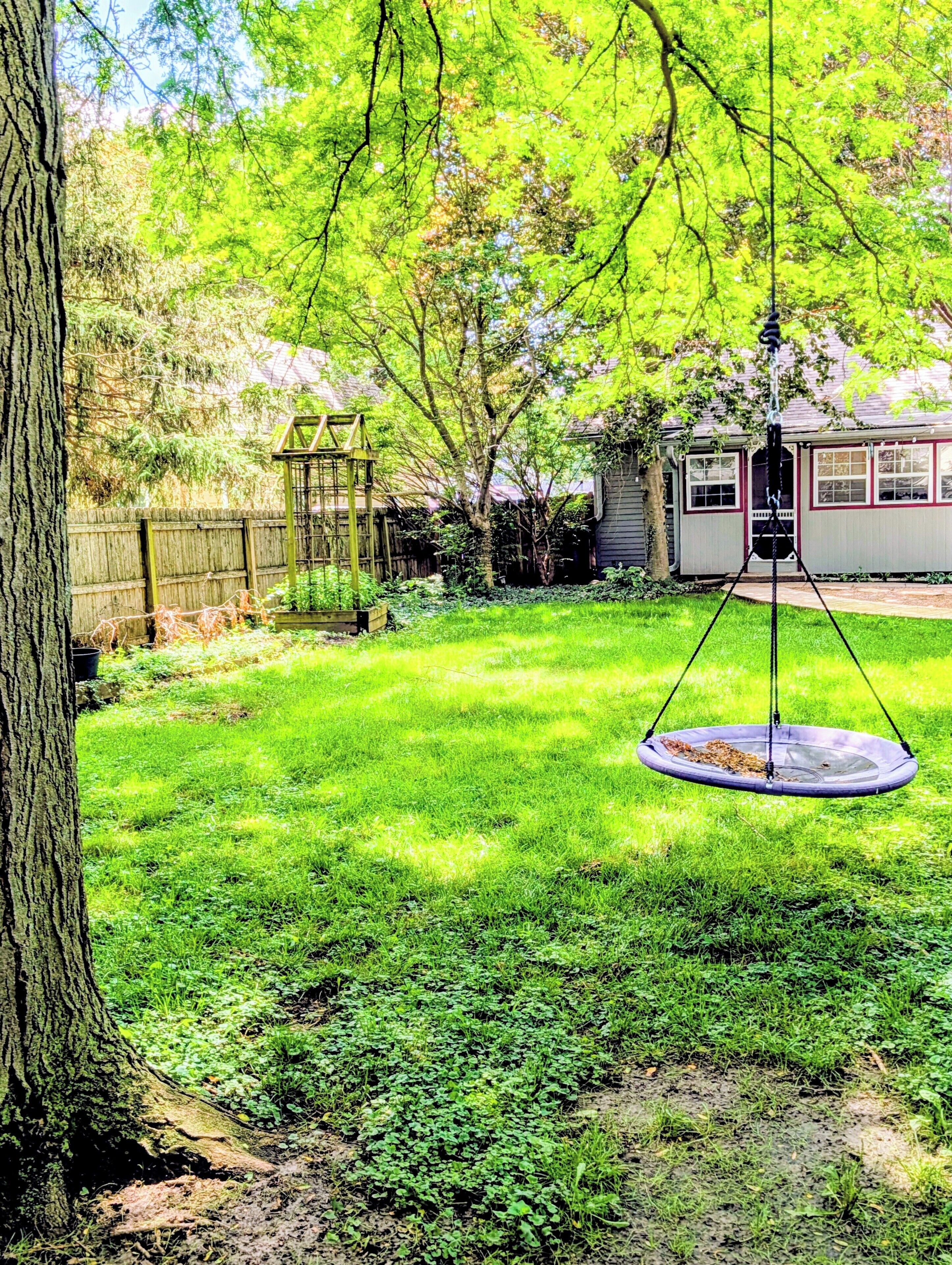 A backyard with a swing set, a wooden fence, and a house in the background.
