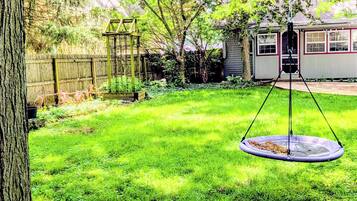 A backyard with a swing set, a wooden fence, and a house in the background.
