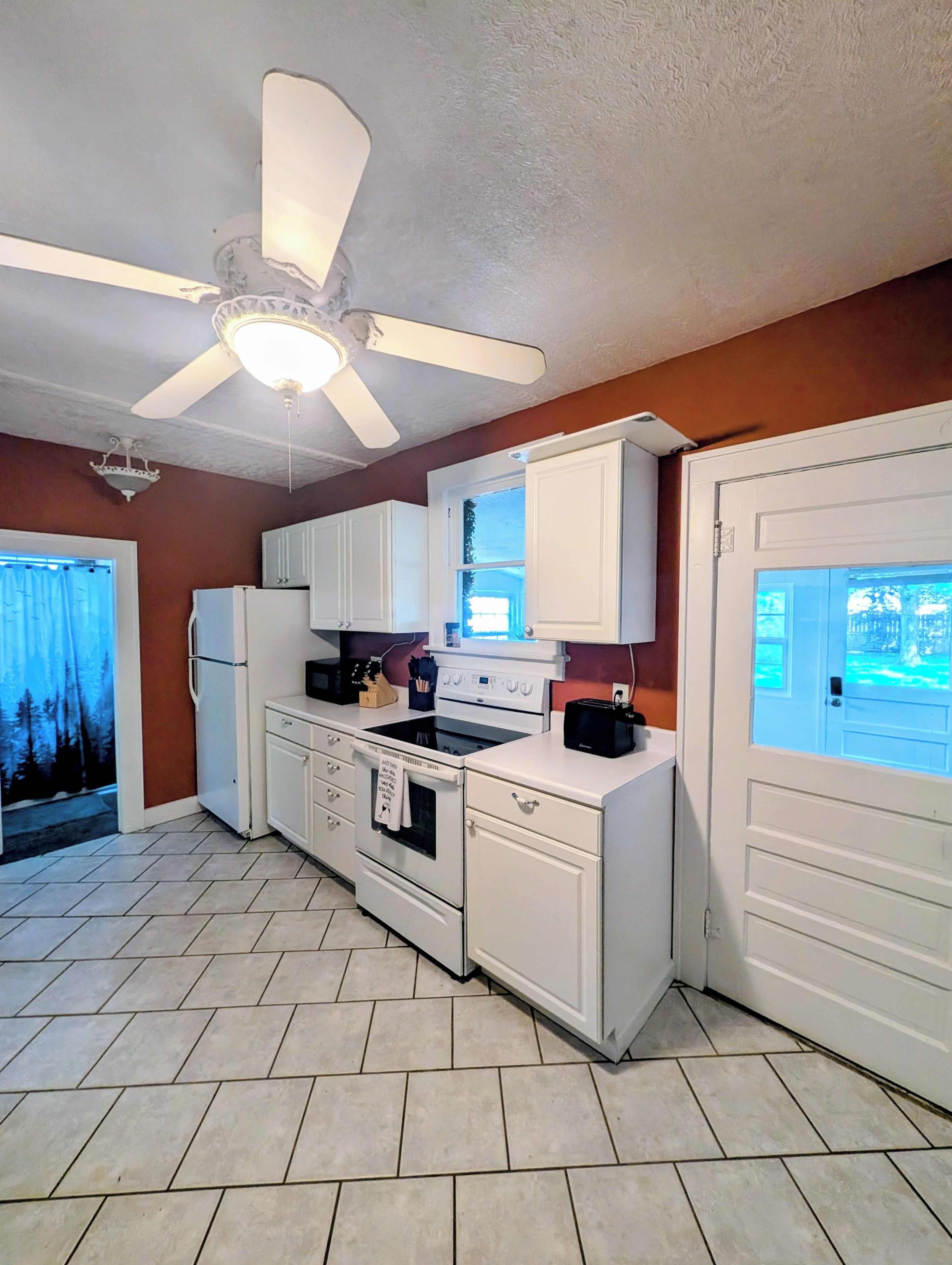 Una cocina con armarios blancos, estufa, ventilador de techo y ventana con vistas.