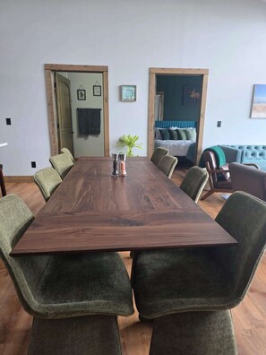 A conference room with a wooden table, green upholstered chairs, a plant, and a blue sofa in the background.