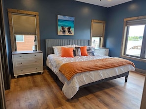 A bedroom with a bed, two nightstands, a painting, and a window.