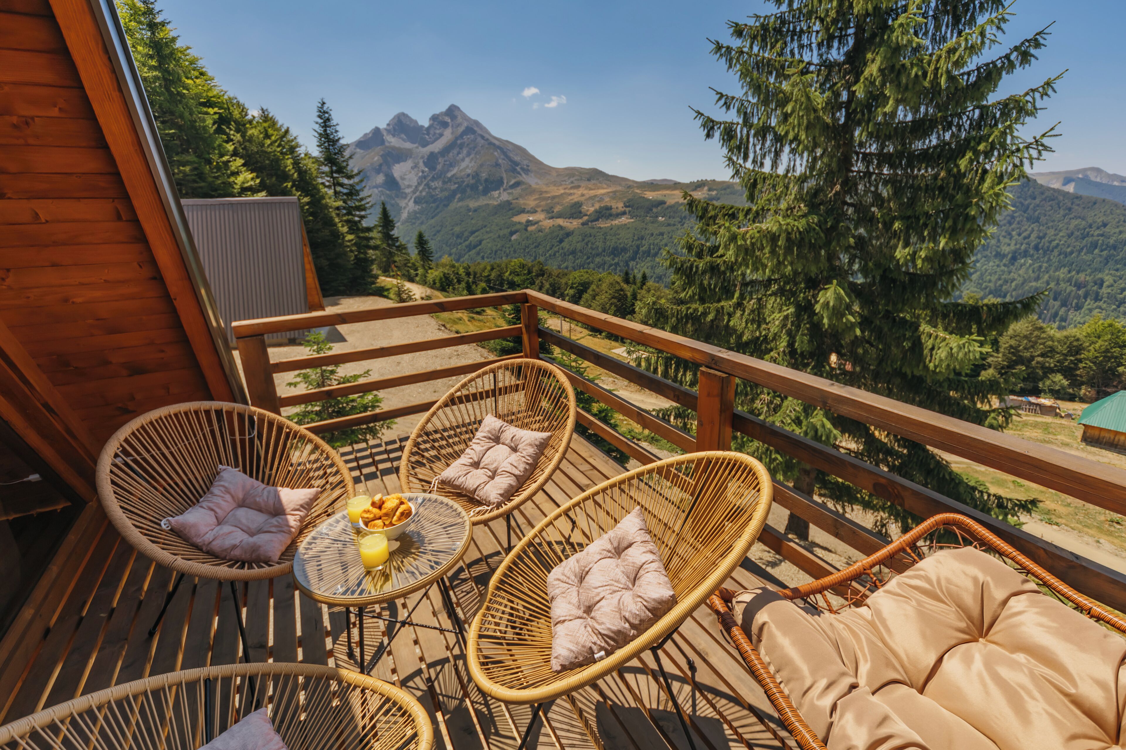 A wooden deck with wicker chairs and a table, overlooking a mountainous landscape.