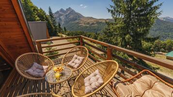 A wooden deck with wicker chairs and a table, overlooking a mountainous landscape.