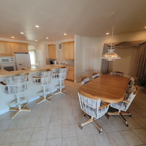 A modern kitchen with a central island, a dining area with a wooden table and chairs, and a chandelier. - Beautiful 4,000 sq ft home at the base of the Colorado National Monument. (Grand Junction)