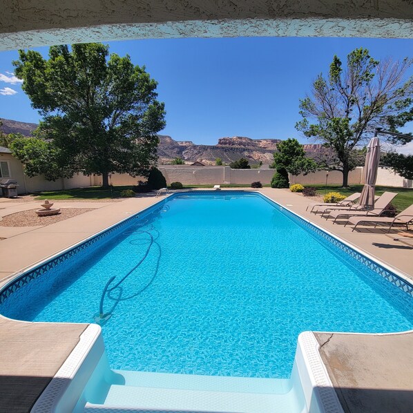 Ein rechteckiger Pool mit klarem, blauem Wasser, umgeben von einer Terrassenanlage mit Liegestühlen und Blick auf eine gebirgige Landschaft.