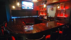 Un área de bar con una barra de madera curva, luces colgantes y una pantalla de televisión.